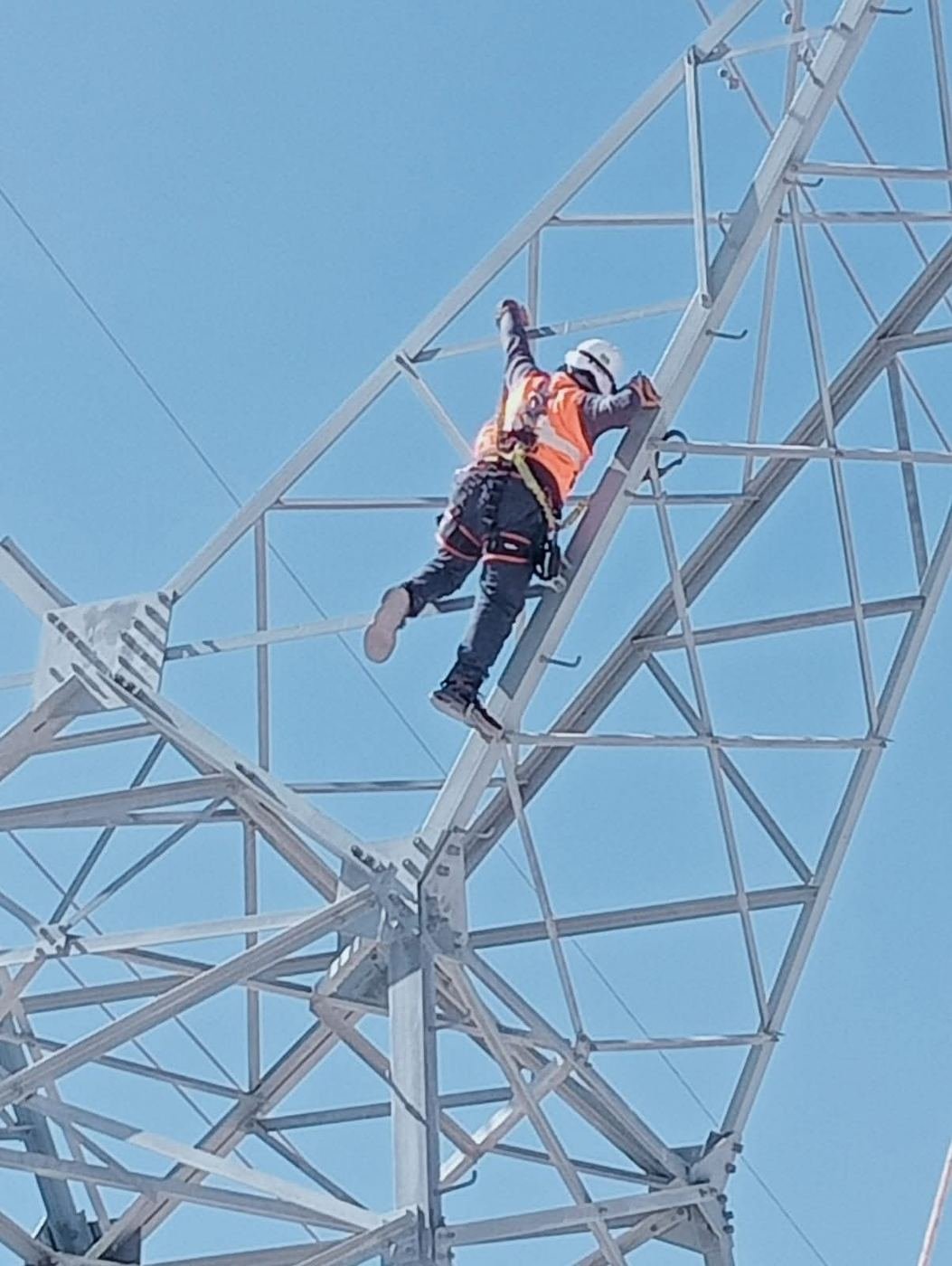 Técnico ascendiendo por una torre de alta tensión con arnés